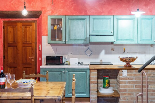 A kitchen with teal cabinets, a wooden door, a microwave, a toaster, and a brick oven.