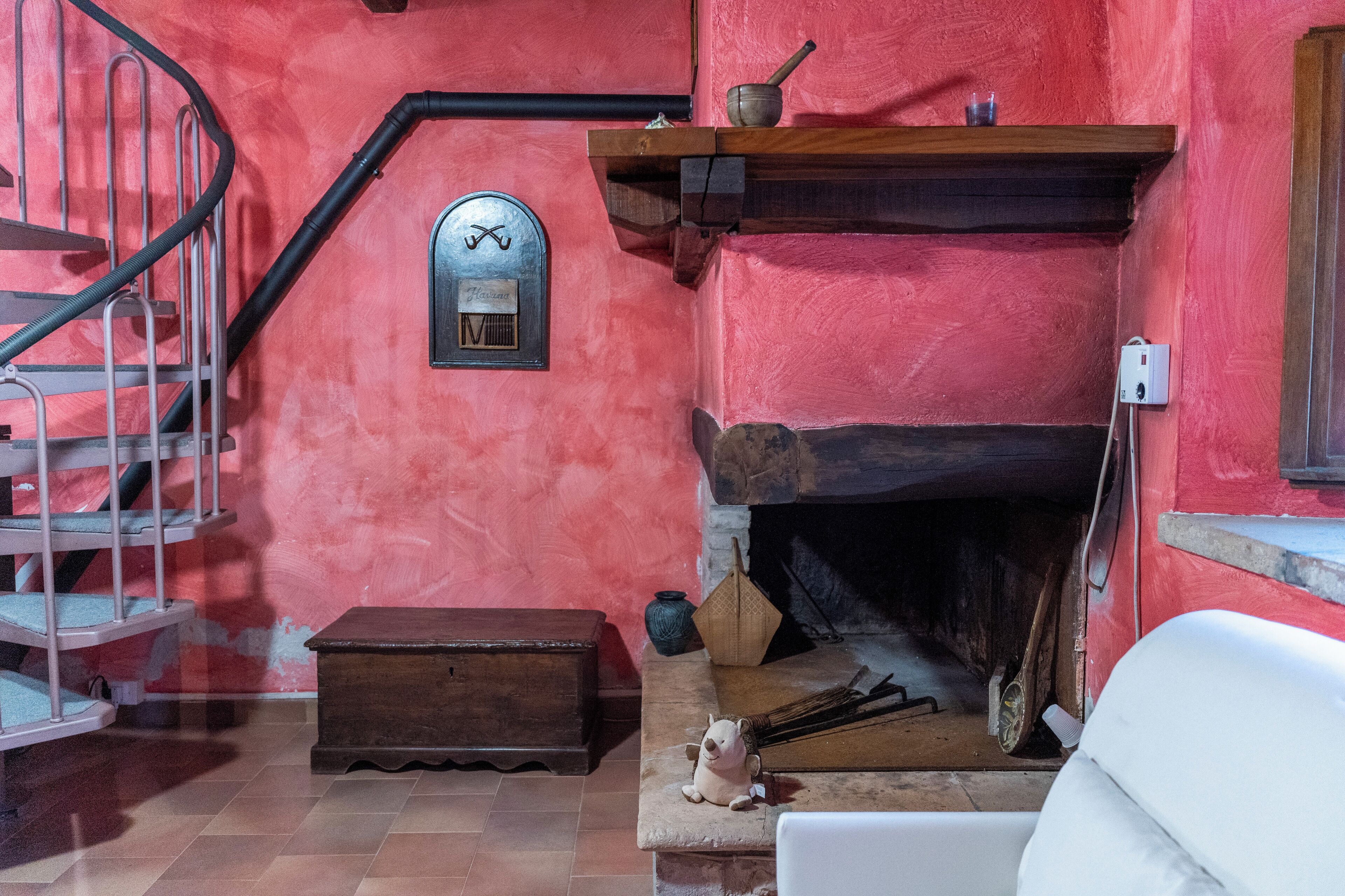 A room with a red wall, a fireplace, a wooden bench, a small table, and a spiral staircase.