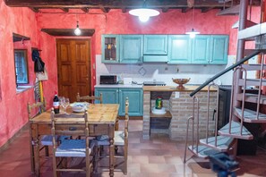 Une cuisine avec des armoires de couleur turquoise, une table à manger en bois et un poêle en briques.
