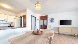 A modern kitchen with white cabinets, a dining table with chairs, a television, and a wicker basket on the table. - El Charcón A • 10 meters to the beach • LVH (Arrieta)