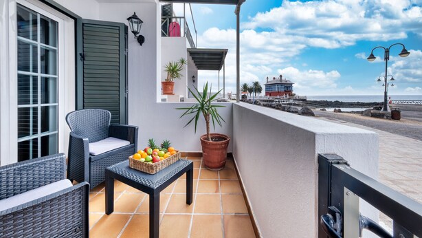 A balcony with wicker furniture, a potted plant, and a fruit basket. - El Charcón A • 10 meters to the beach • LVH (Arrieta)