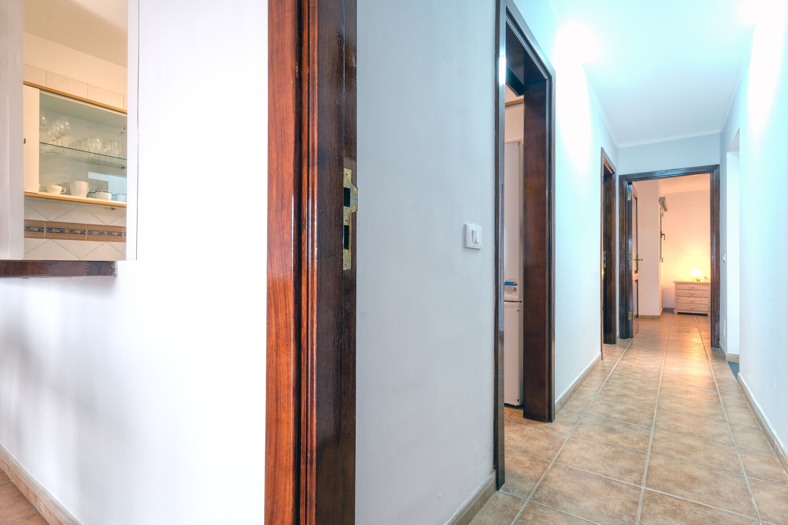 A hallway with a wooden door frame, a tiled floor, and a light fixture on the wall.