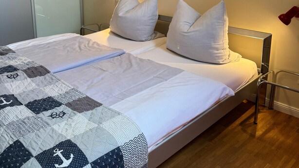 A neatly made bed with a quilt, a painting on the wall, and a bedside lamp. - Apartment 'Moderne 2 Pers' with Private Terrace, Shared Garden and Wi-Fi (Bad Zwischenahn)