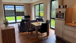 Una cocina moderna con horno Bosch, un comedor con mesa y sillas, y ventanas grandes con cortinas.