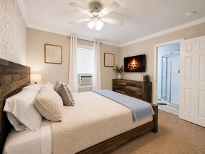 A bedroom with a wooden headboard, a bed with white bedding, a ceiling fan, a fireplace, and a TV. - Stylish Modern Apt Near Northside Hospital (Cumming)