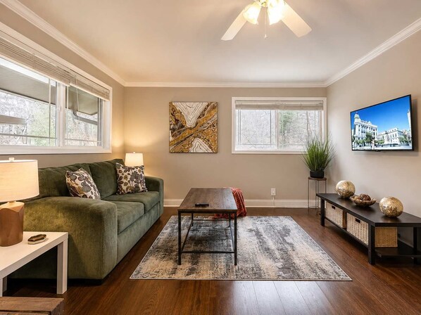 A living room with a sofa, coffee table, and TV. - Stylish Modern Apt Near Northside Hospital (Cumming)