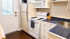 Una cocina con armarios blancos, estufa, microondas y fregadero.