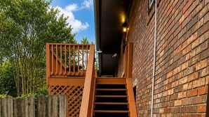 Una escalera de madera que conduce a un edificio de ladrillo, con una valla de madera y follaje.