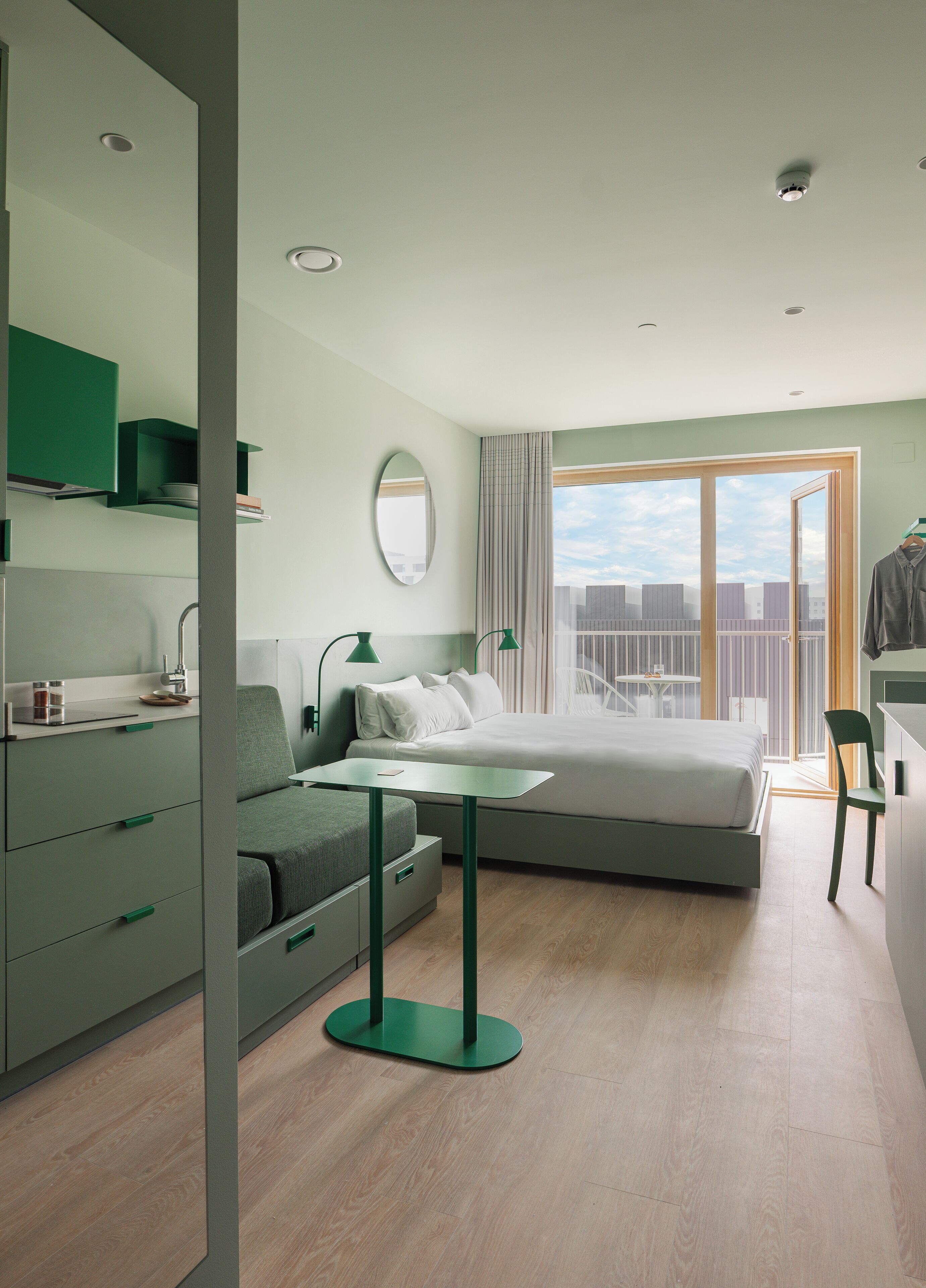 Habitación de hotel moderna con cama, escritorio, silla y balcón con vista a la ciudad.
