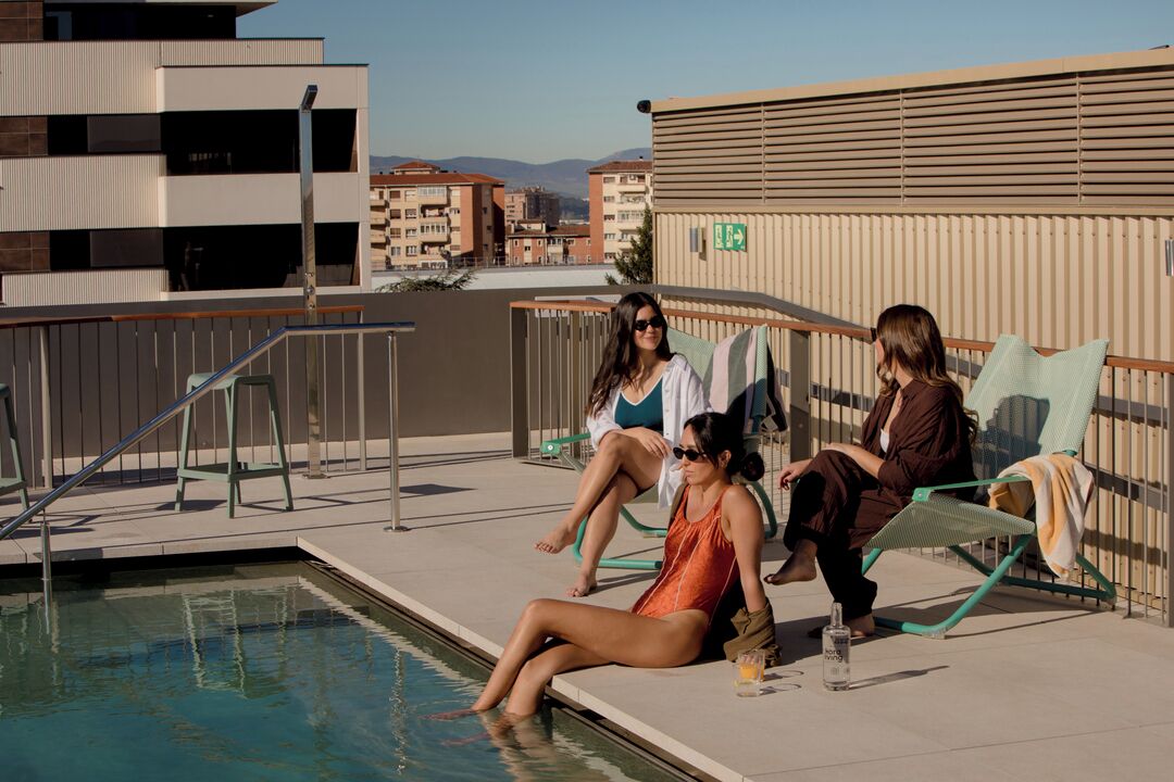 A rooftop pool area with a pool, lounge chairs, and a view of buildings in the background.