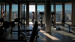 Un gimnasio con equipo de ejercicio y amplias ventanas que ofrecen vistas a la ciudad.