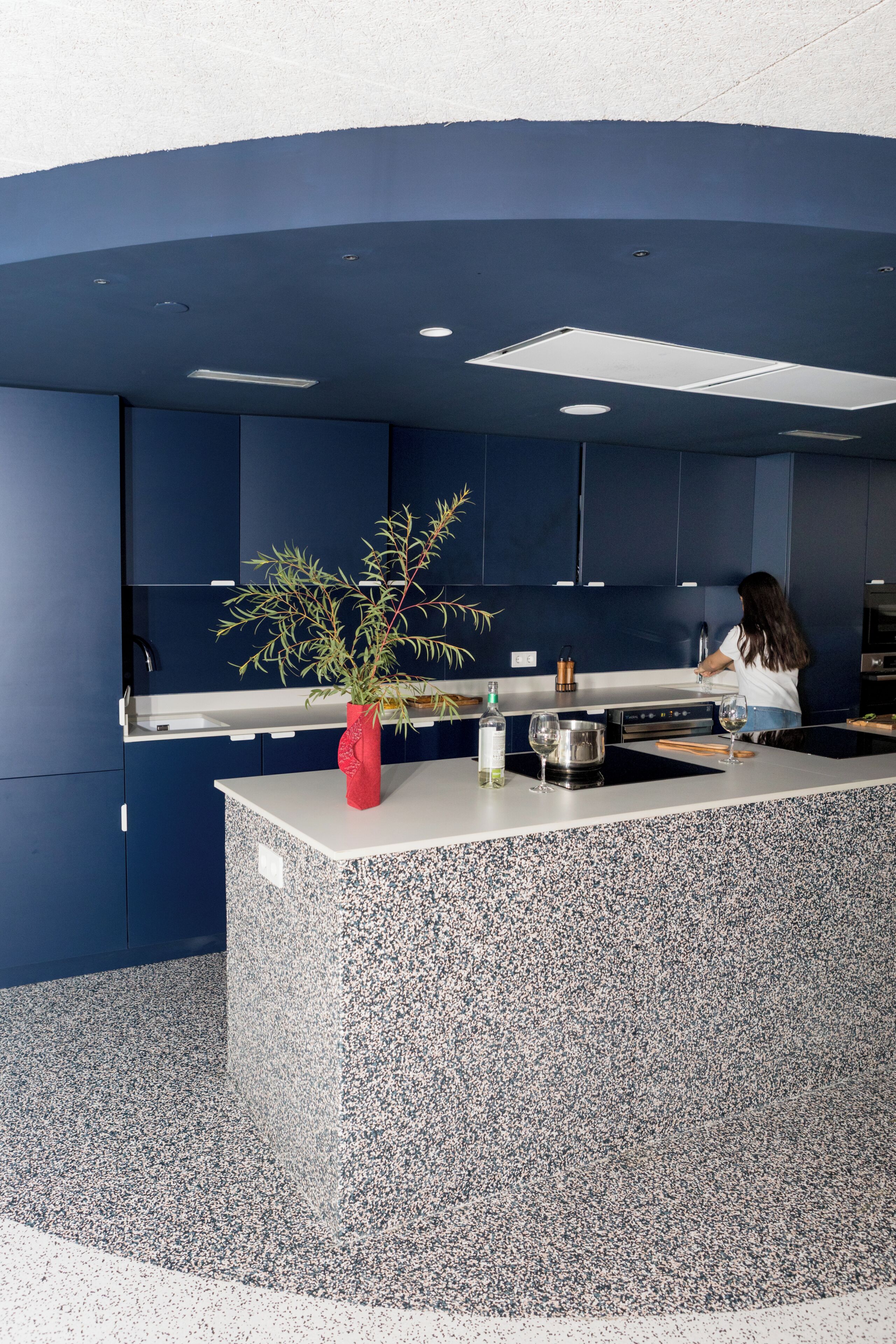 Una cocina moderna con armarios azul oscuro, encimera de granito y un florero rojo con una planta.