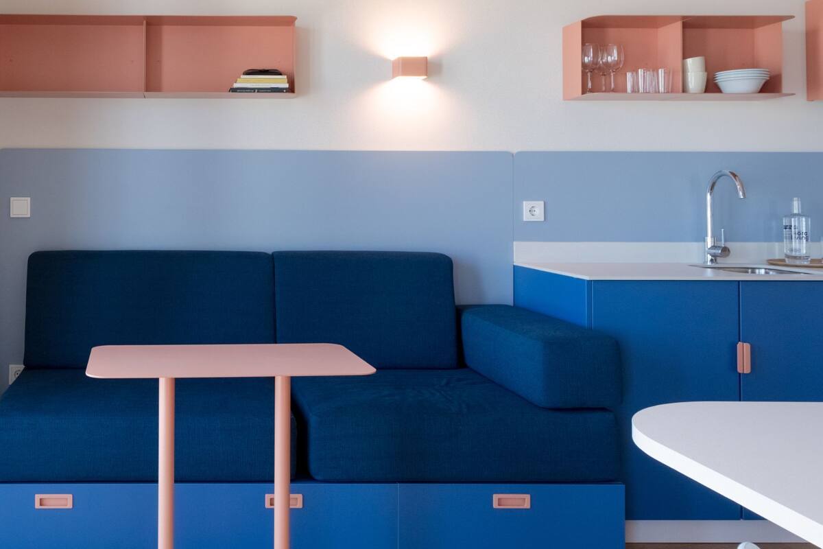 A modern kitchenette with a blue sofa, a small table, and pink cabinets.