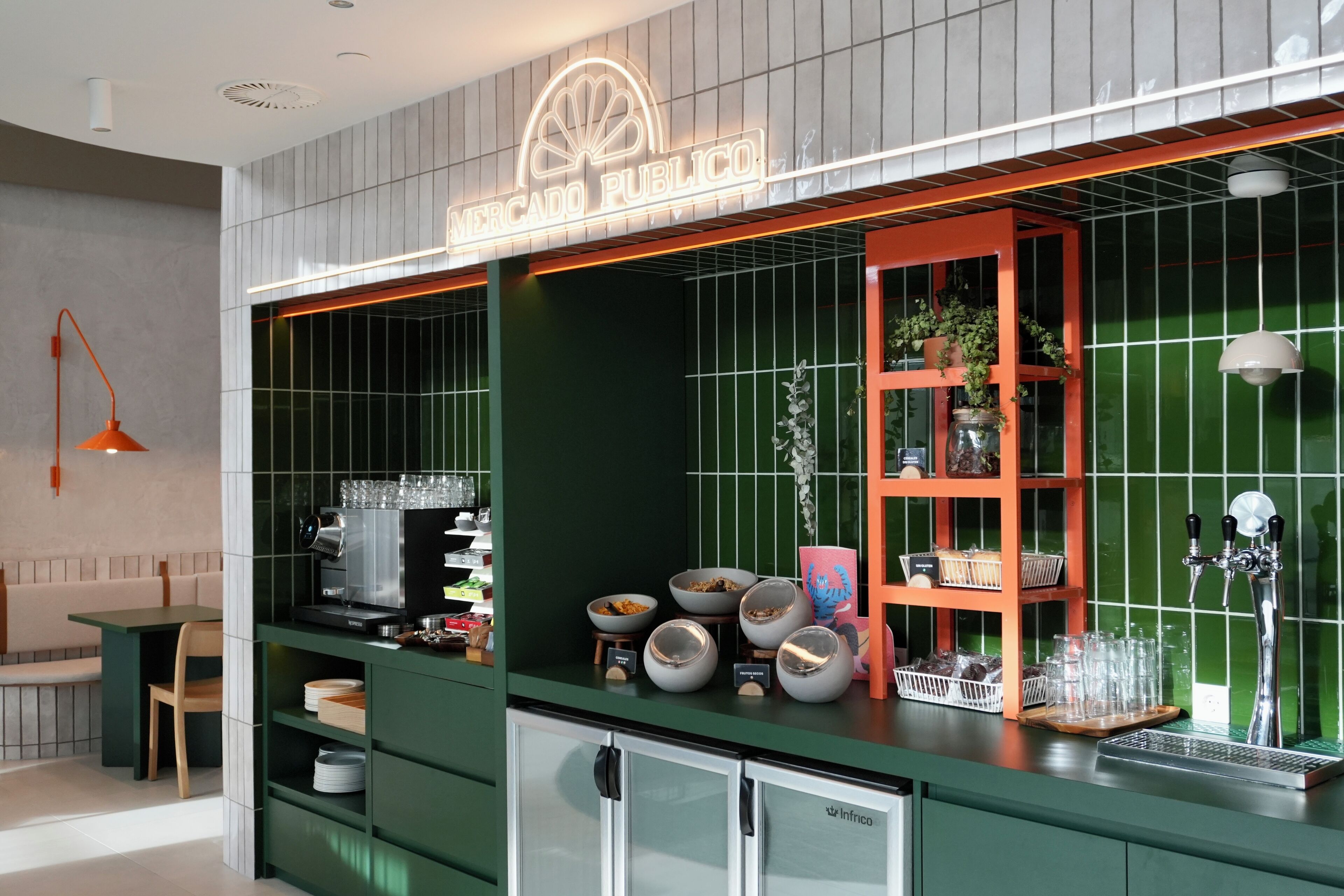 Un área de bar moderna con un letrero de neón, paredes con azulejos verdes y una variedad de copas y recipientes sobre la barra.