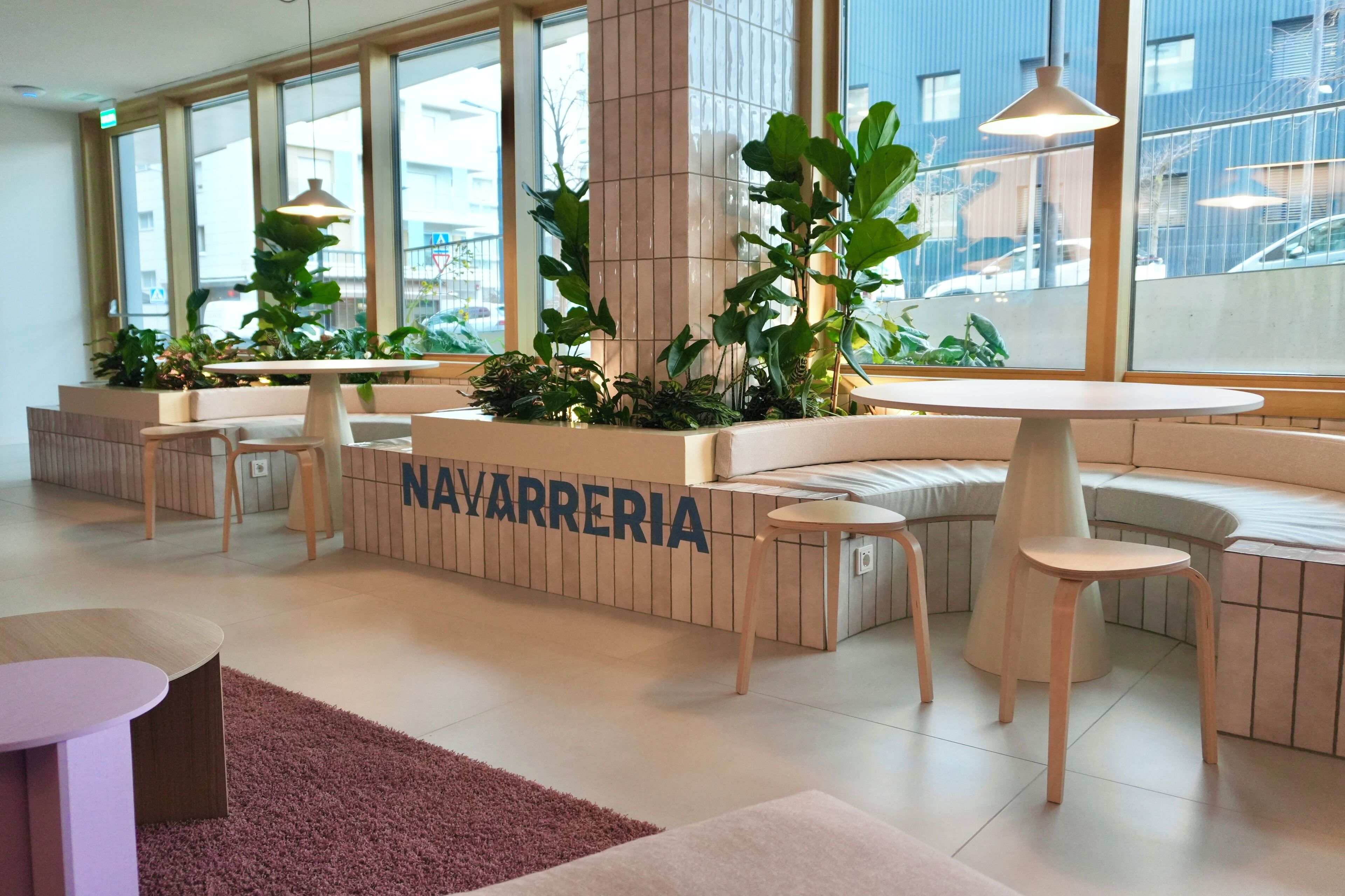 A modern, well-lit lobby with seating areas, large windows, and indoor plants.