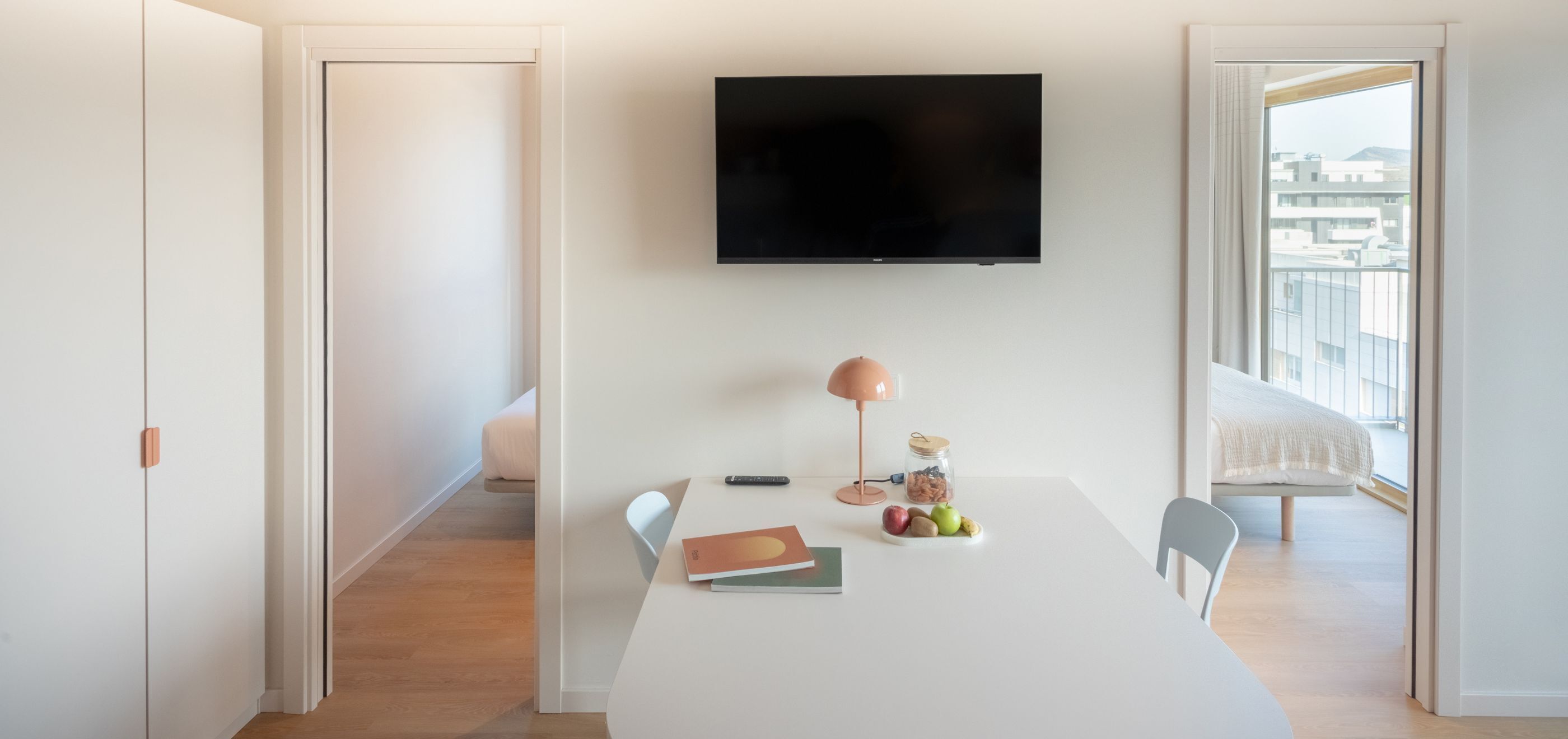Een moderne kamer met een flatscreen televisie, een witte tafel met een lamp, een boek en fruit.