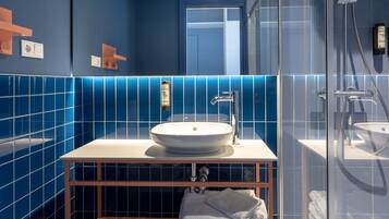 Une salle de bain moderne avec un lavabo blanc, des murs recouverts de carreaux bleus, une douche en verre et un meuble-lavabo en bois.