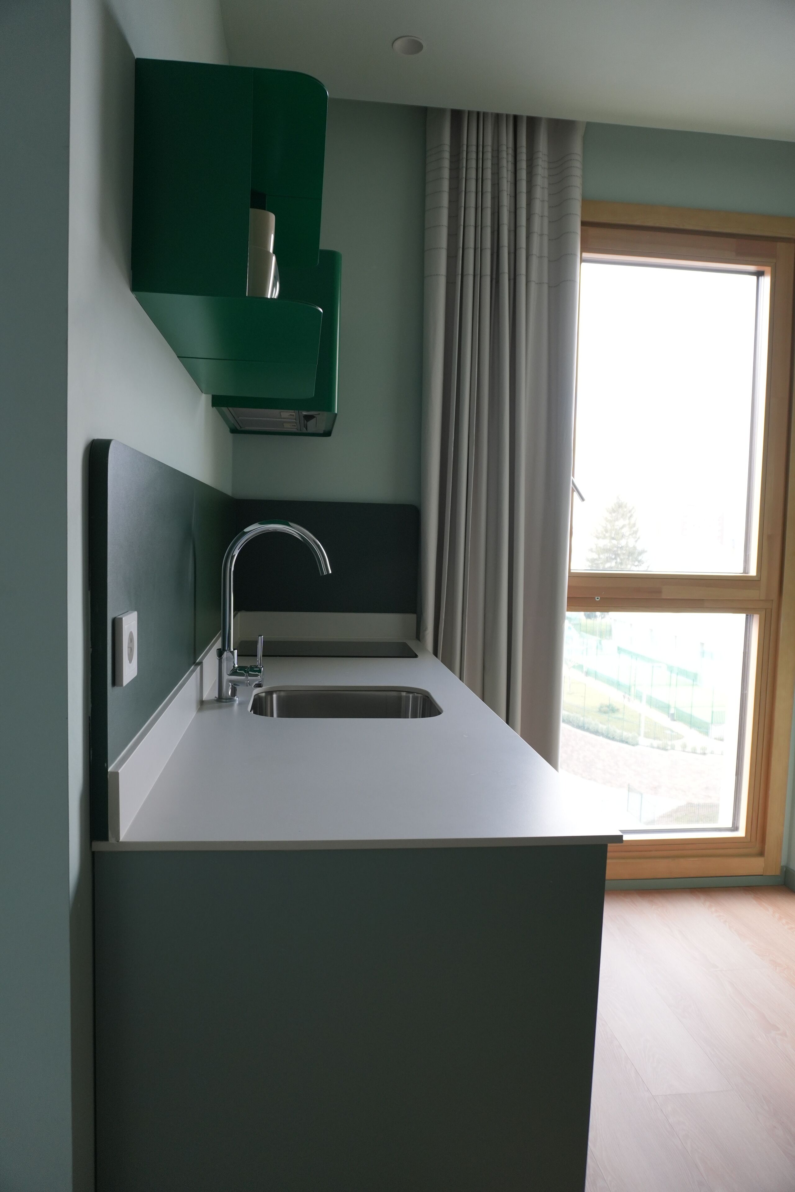 A modern kitchen with a built-in sink, a green cabinet, and a large window with curtains.