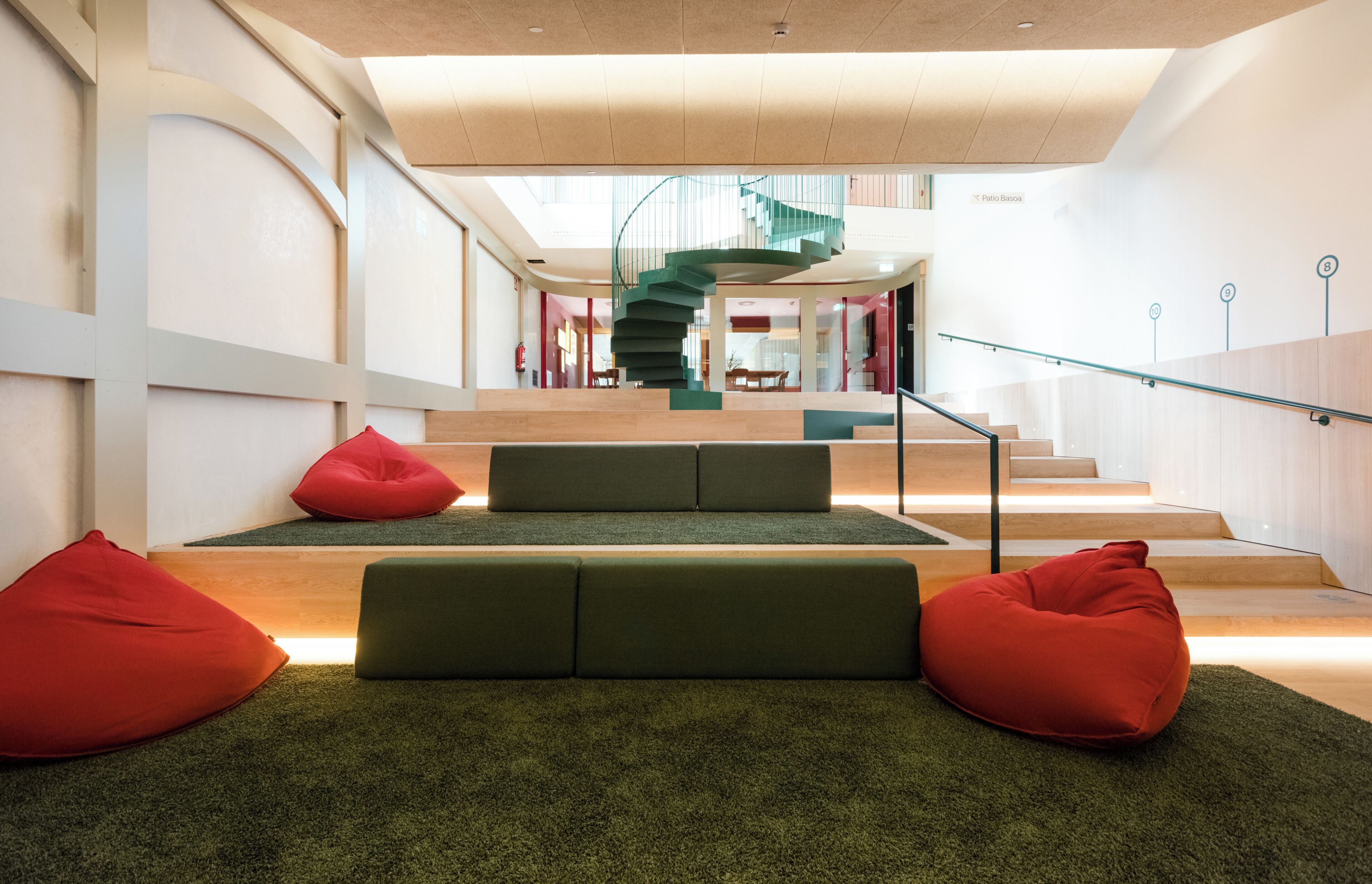 Un interior moderno con una escalera en espiral, asientos verdes y suelo de madera.