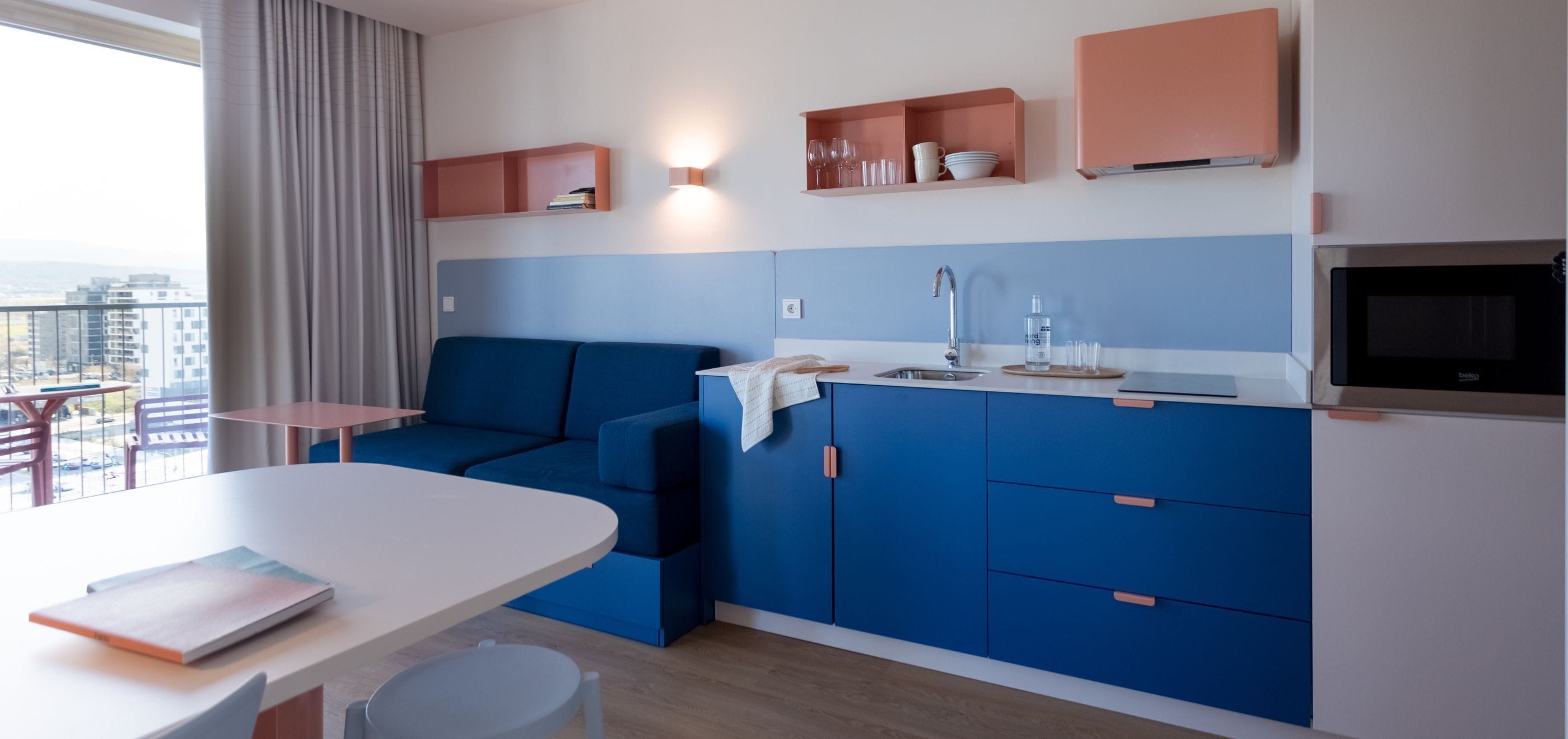 A modern kitchen with blue cabinets, a white countertop, and a built-in microwave.