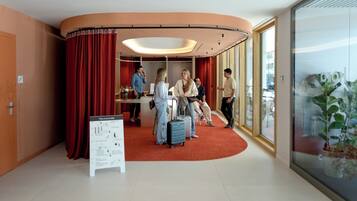 Un hall d’hôtel avec un tapis rouge incurvé, un comptoir d’accueil et une grande fenêtre donnant sur un beau paysage.