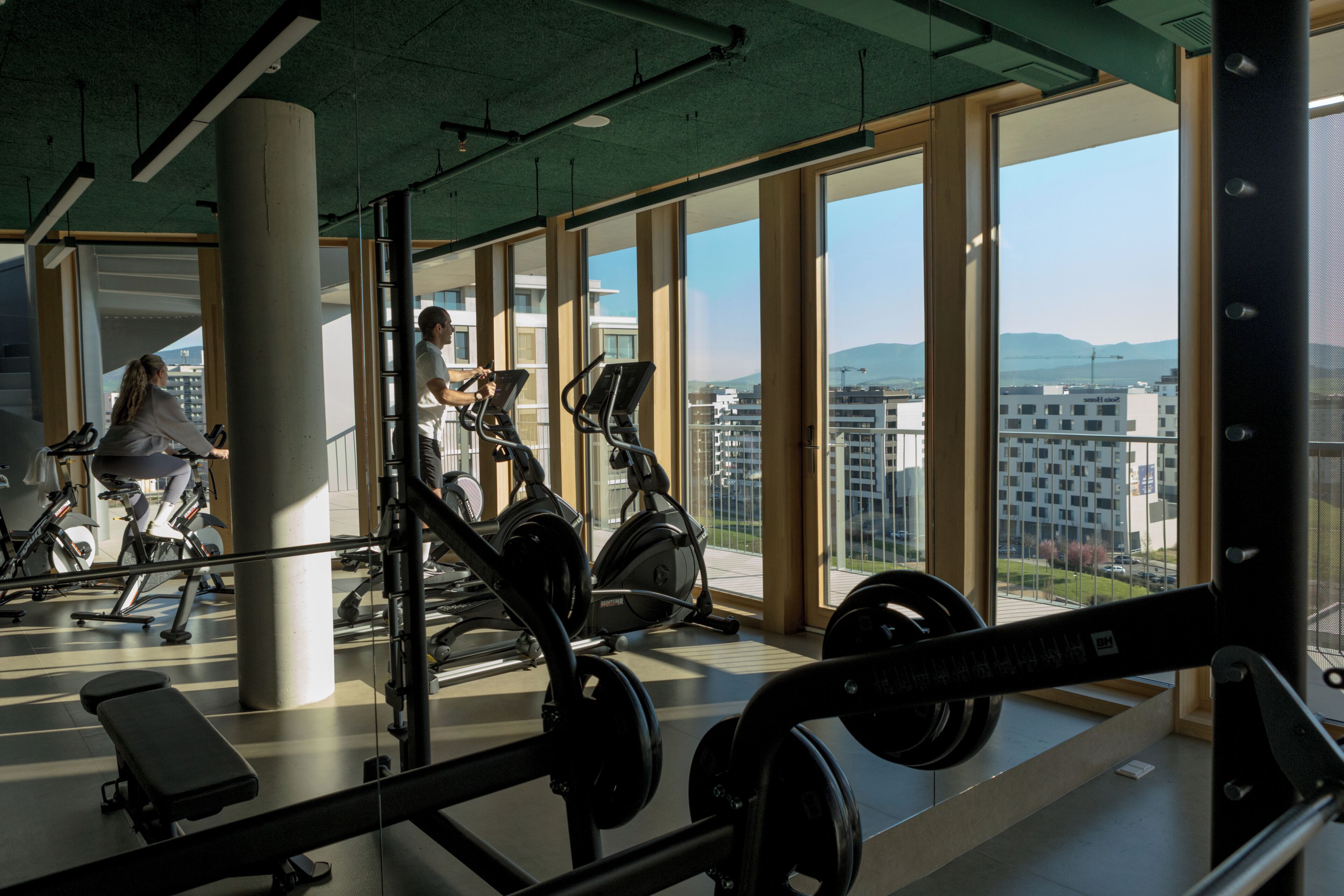 A gym with exercise equipment, large windows, and a view of buildings.