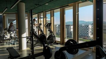 A gym with exercise equipment, large windows, and a view of buildings.