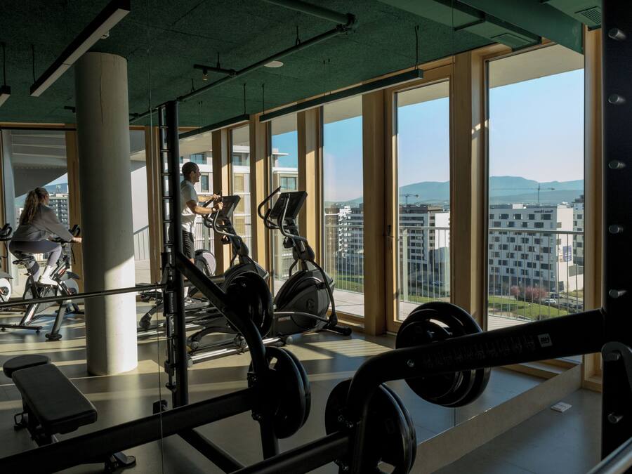 A gym with exercise equipment, large windows, and a view of buildings.