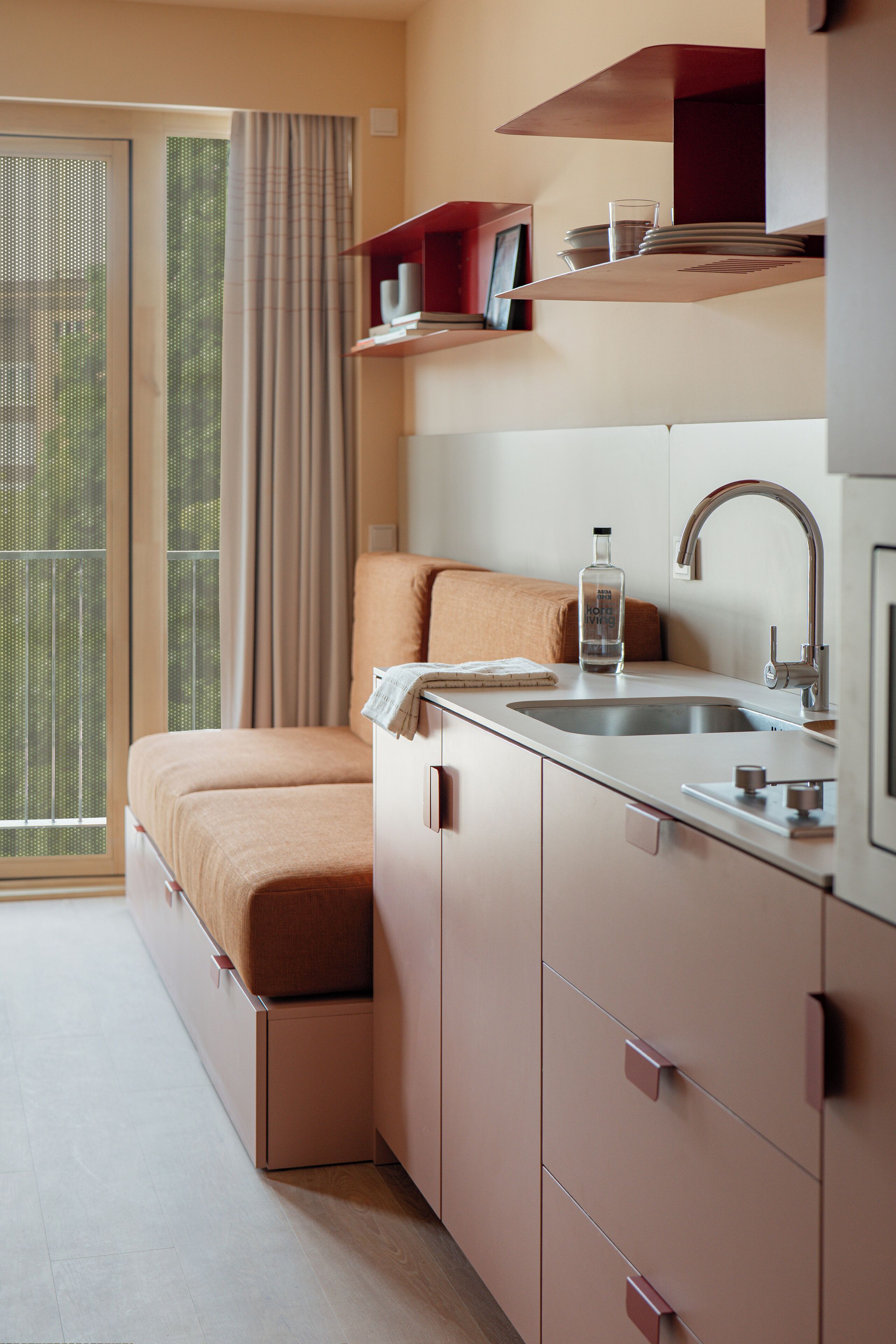 Een kleine kamer met een bed, een wastafel en een raam met gordijnen.