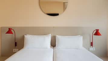 Una cama doble con ropa de cama blanca, dos lámparas de noche rojas y un espejo redondo en la pared.