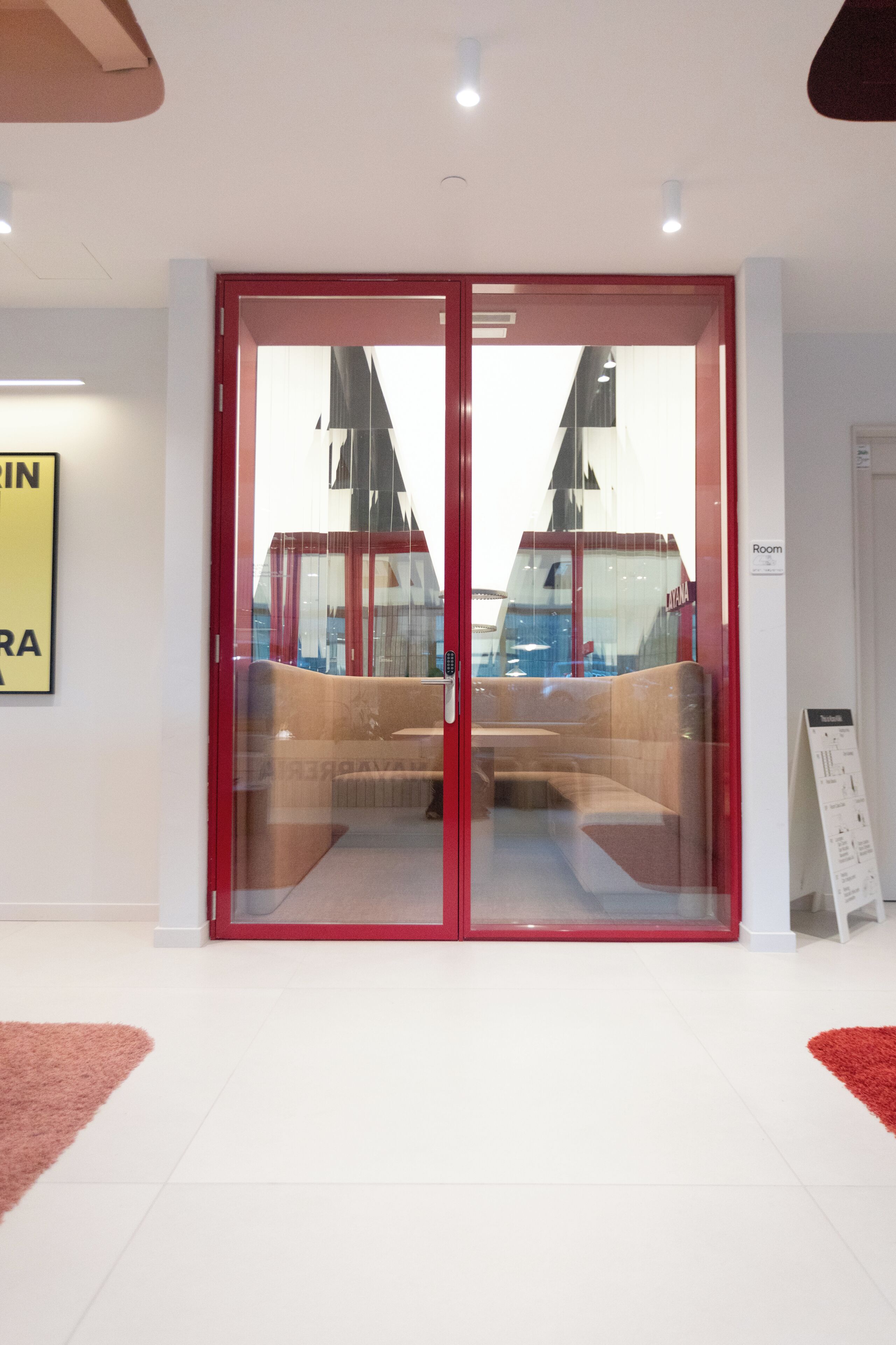 A modern hotel lobby with a glass door entrance, a seating area with a sofa and chairs, and a sign indicating the room number.