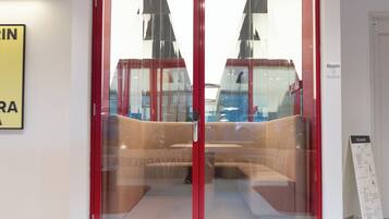 A modern hotel lobby with a glass door entrance, a seating area with a sofa and chairs, and a sign indicating the room number.