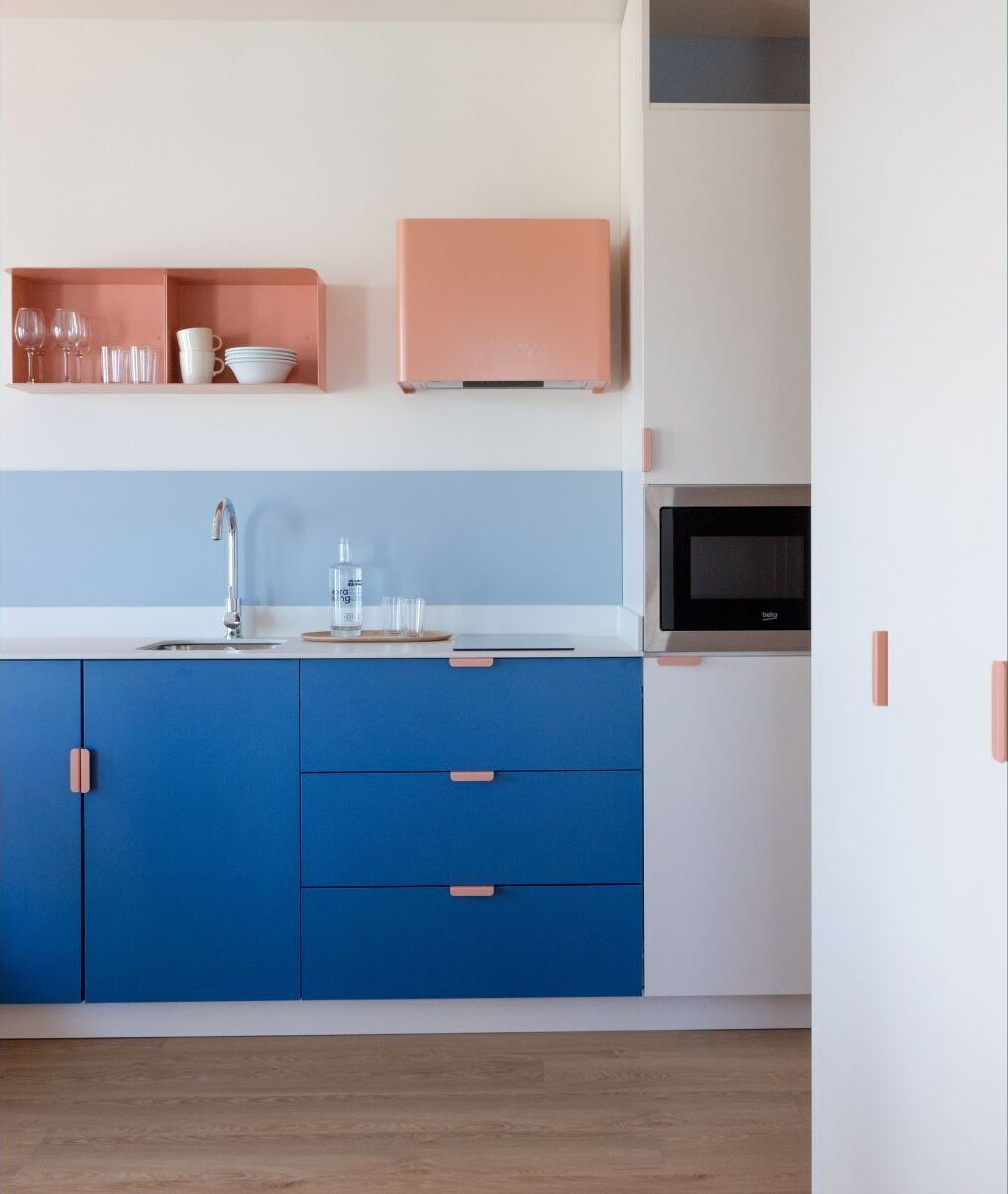 Una cocina moderna con armarios azules, encimera blanca y estante rosa.