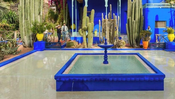 A courtyard with a fountain, cacti, and a blue building with arches. - Apartment Marrakech Menara (Marrakesh)