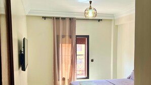 A hotel room with a bed, a ceiling fan, a window with curtains, and a door. - Apartment Marrakech Menara (Marrakesh)