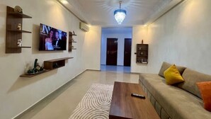 A modern living room with a flat-screen TV, wooden shelves, a sofa with cushions, and a patterned rug. - Apartment Marrakech Menara (Marrakesh)