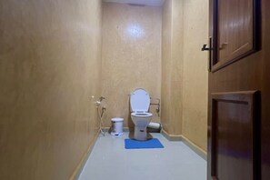 A small bathroom with a toilet, a blue mat, and a wooden door.