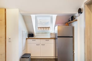 Eine kleine Küche mit Fenster, Kühlschrank, Mikrowelle und Kaffeemaschine.