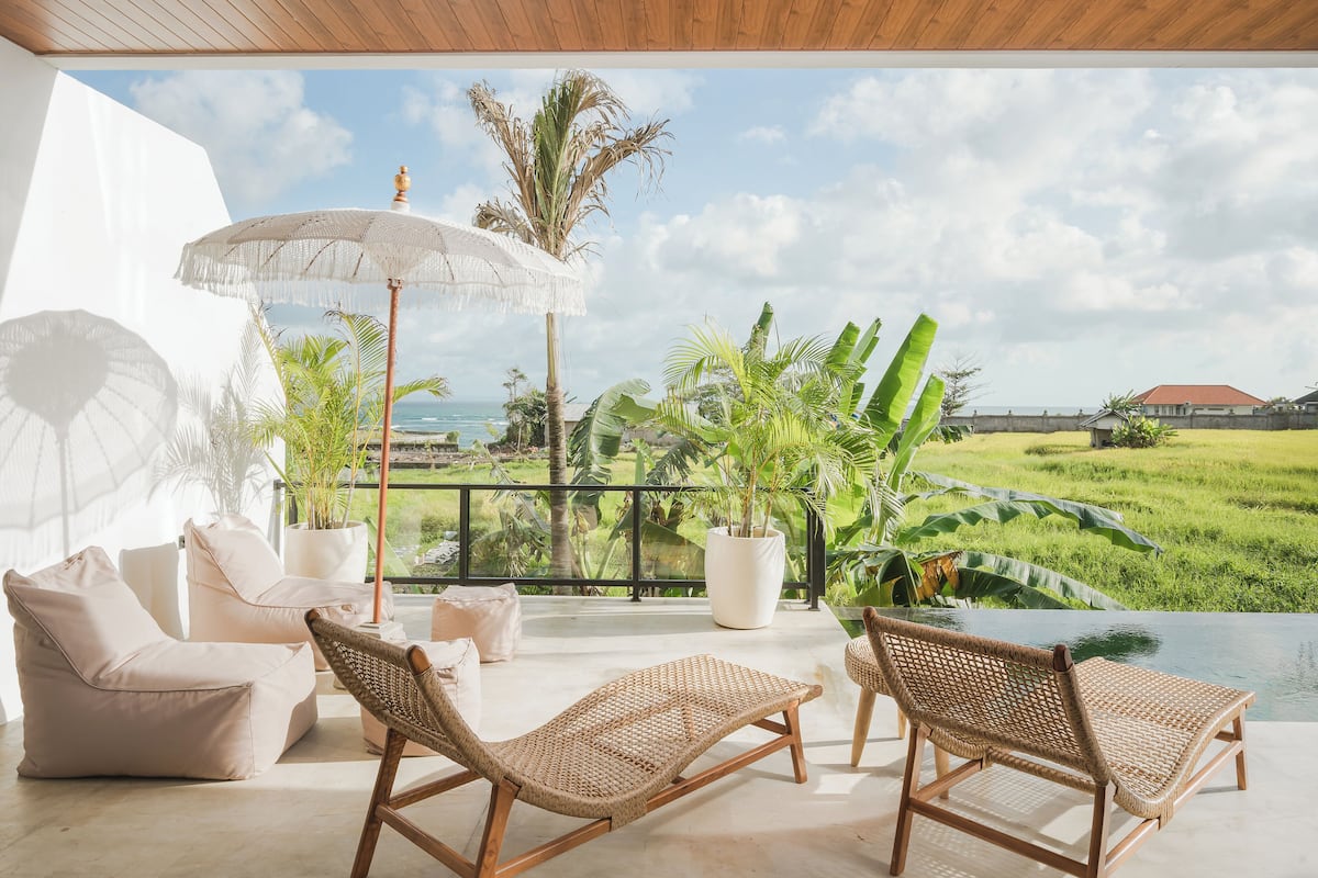 Ein Balkon mit Korlounge-Stühlen, einem weißen Sonnenschirm und Blumentöpfen.