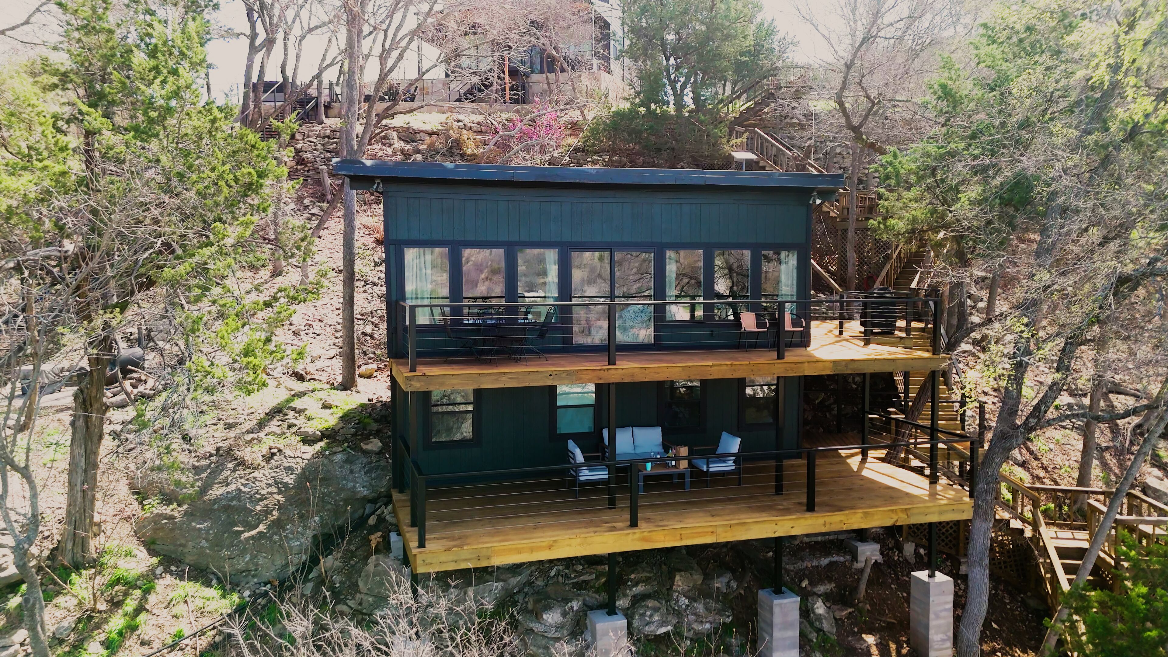 A two-story cabin with a balcony, surrounded by trees.