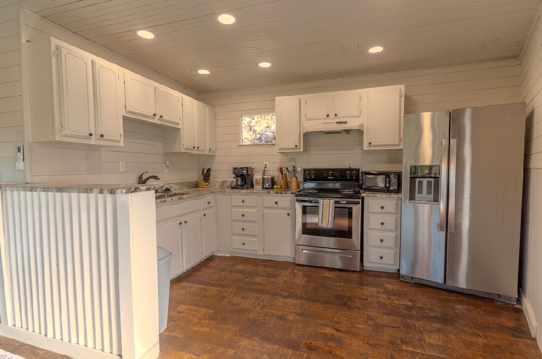A kitchen with white cabinets, stainless steel appliances, and a wooden floor.