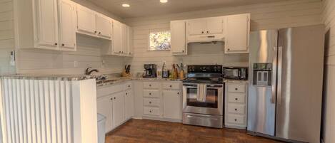 A kitchen with white cabinets, stainless steel appliances, and a wooden floor.