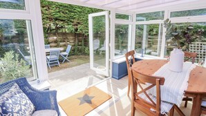 Une véranda à espace ouvert, avec une table et des chaises en bois, un canapé bleu et un tapis en forme d’étoile.