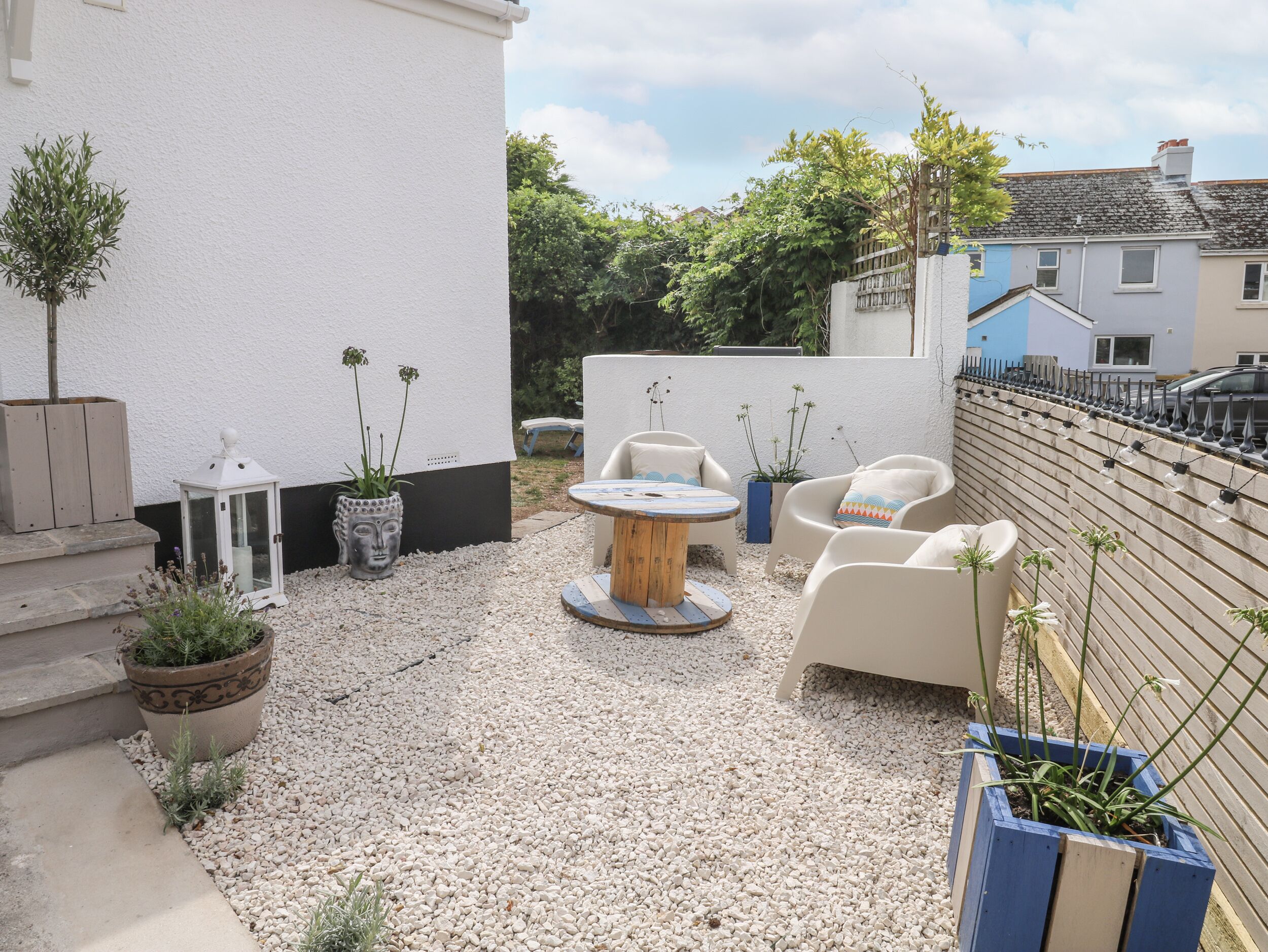 A patio with a round table and four chairs, surrounded by potted plants and a gravel ground.