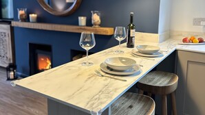Une cuisine avec un plan de travail en marbre, des verres à vin, une bouteille et un panier de fruits.