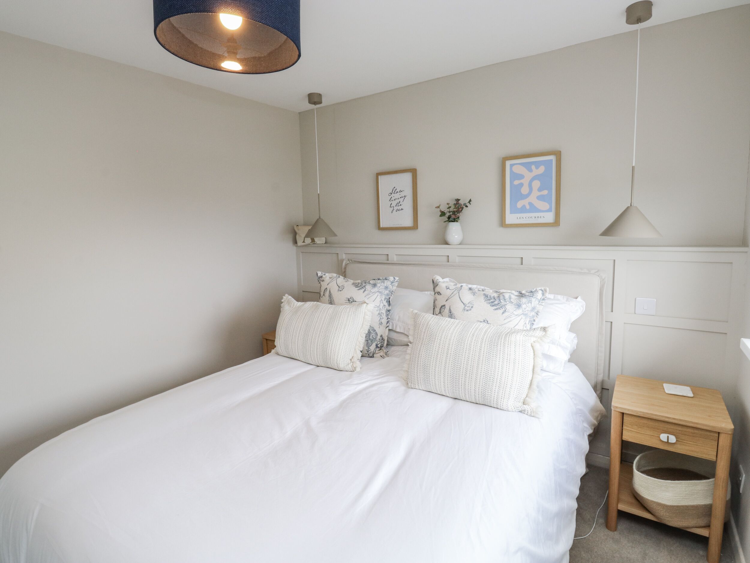 A bedroom with a large bed, a bedside table, a lamp, and two framed pictures on the wall.