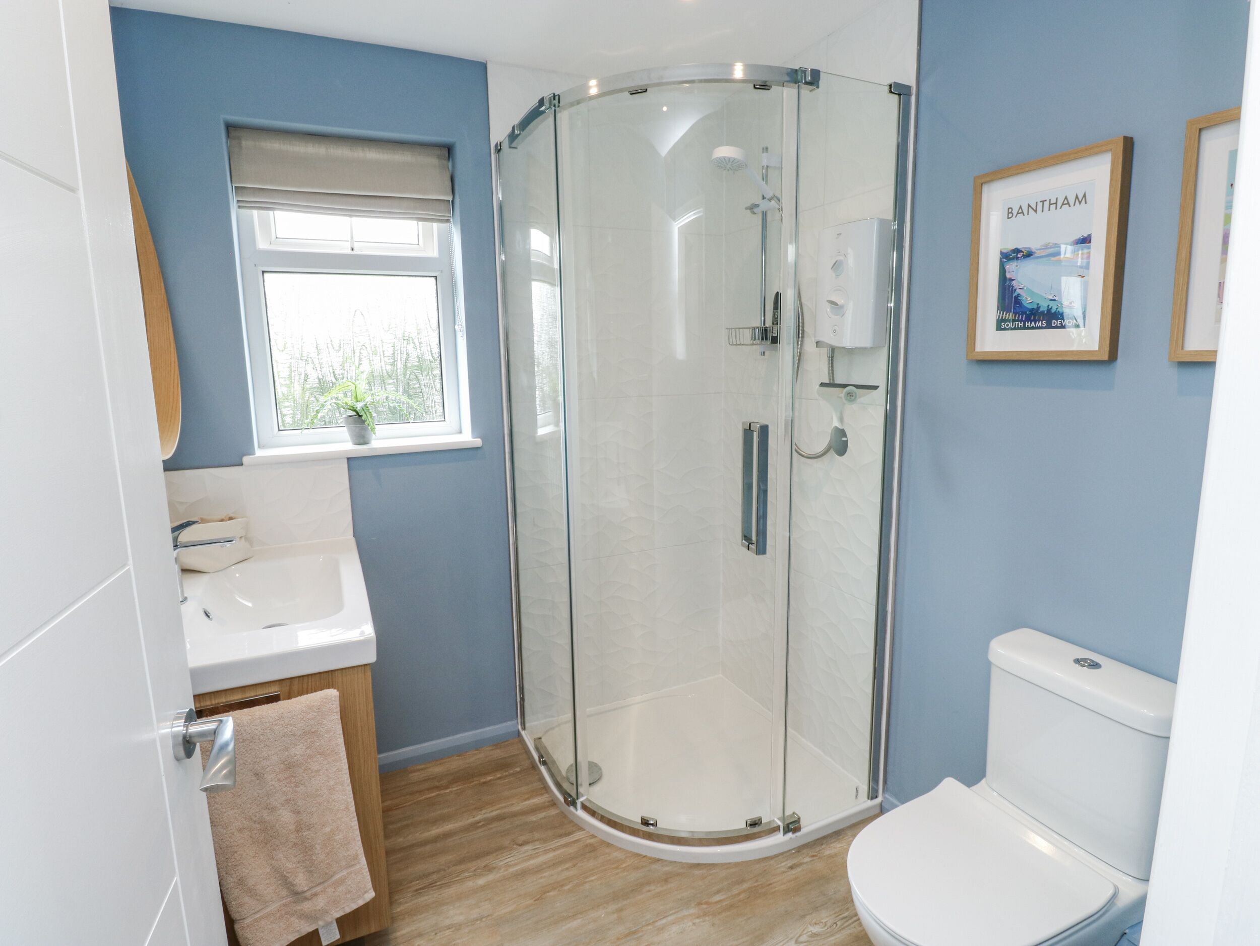 A modern bathroom with a glass shower enclosure, a sink, a toilet, and a window with a view of greenery.