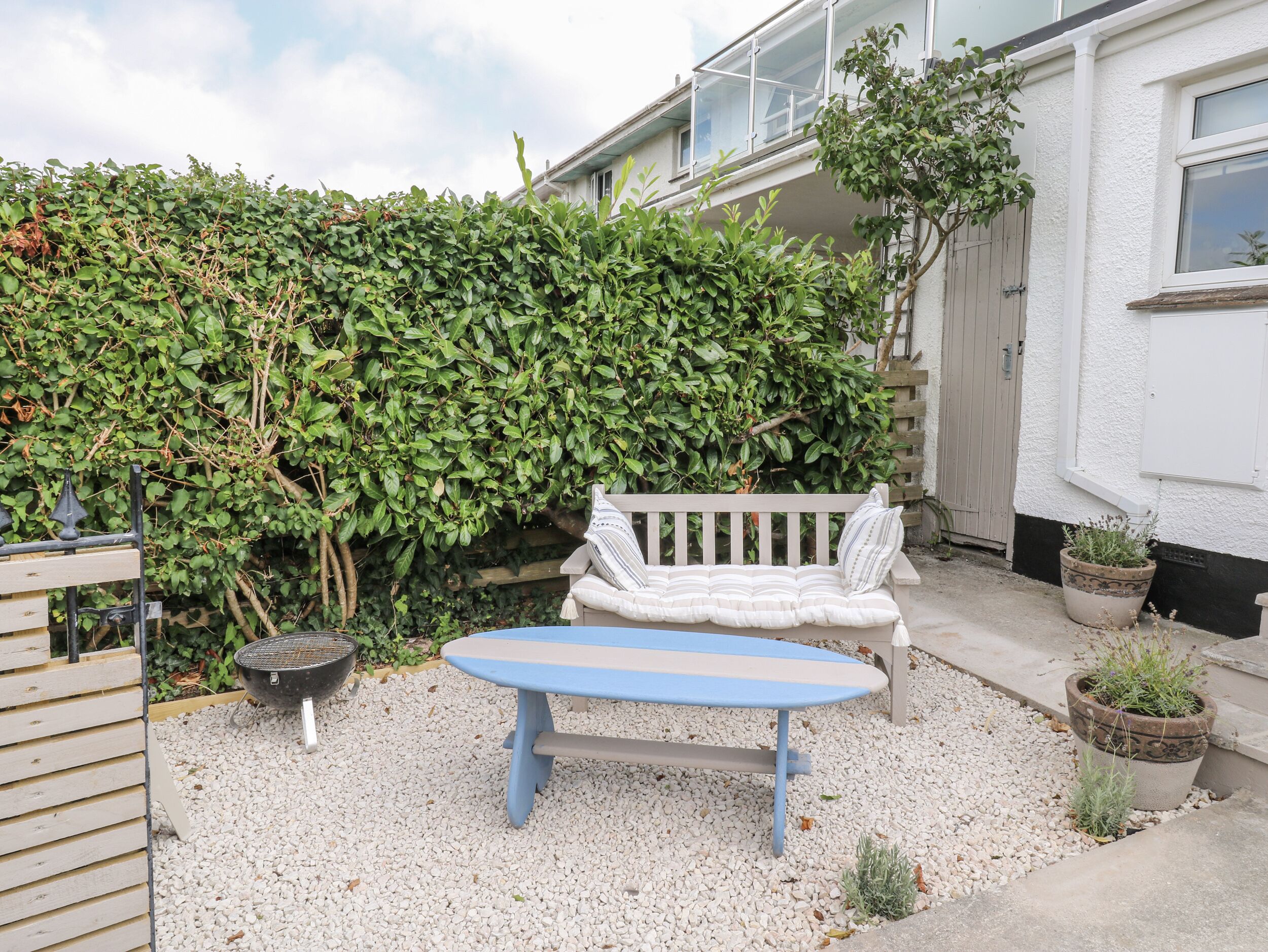 A patio area with a white bench, a blue table, and a grill.