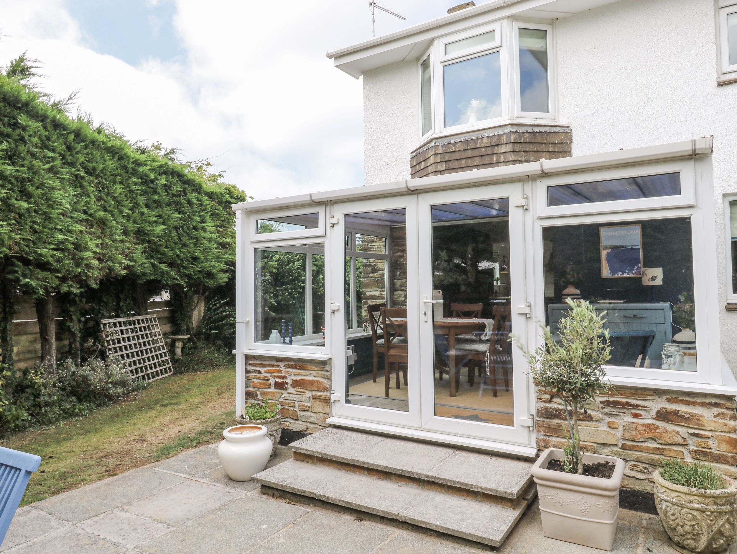 A house with a glass conservatory, stone steps, and potted plants.