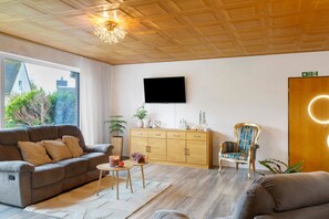 Un salon moderne avec un canapé, un fauteuil et un téléviseur fixé au mur.